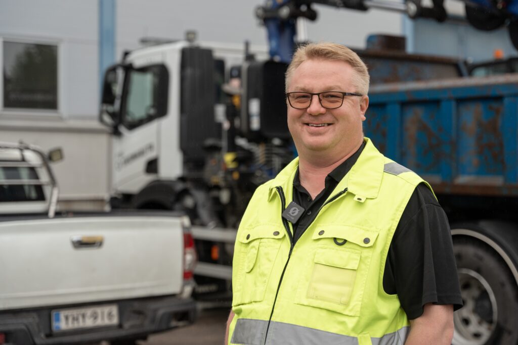 Yrittäjä huomioliivi päällään, taustalla kuorma-auto ja pickup.